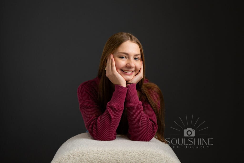 Senior graduation photo of a girl with her chin in her hands. Gray background.