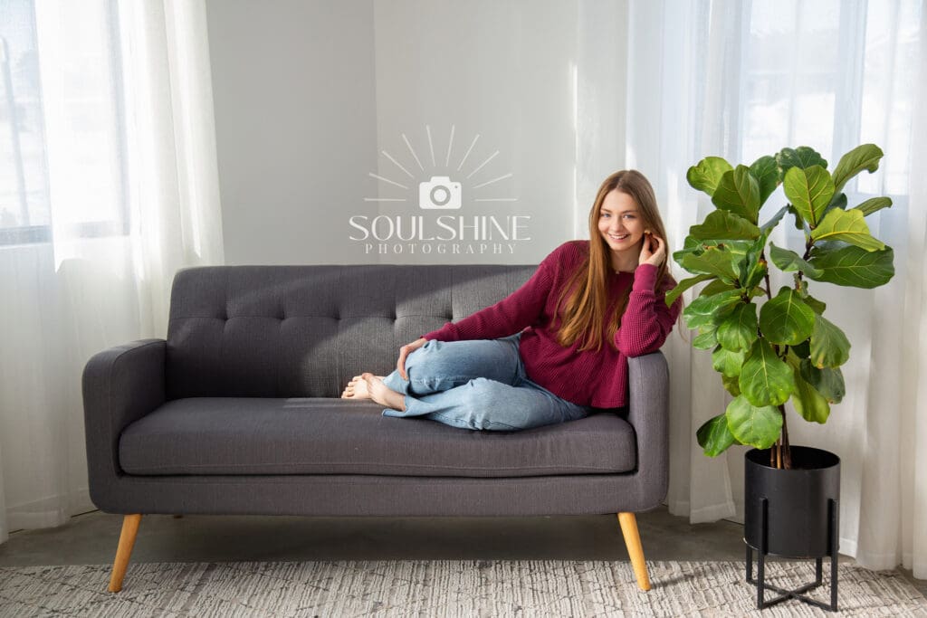 Senior photo of a girl sitting on a couch. Ficus Next to her.